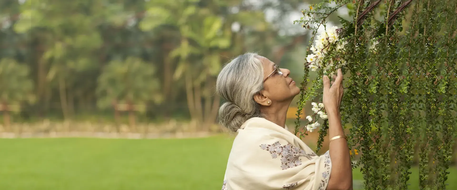 A resident of Jagriti Dham reaching up to a flowering trellis in the garden, with the lawn behind her