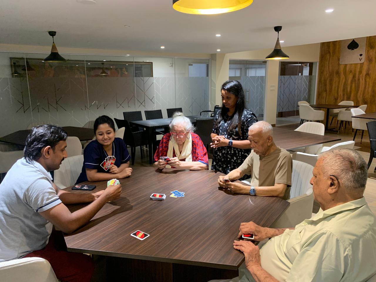 Residents and staff enjoy a lively card game in a modern common area, a typical social scene at one of the premier luxury old age homes in Kolkata.