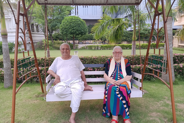 An elderly couple sits on a white porch swing in a garden
