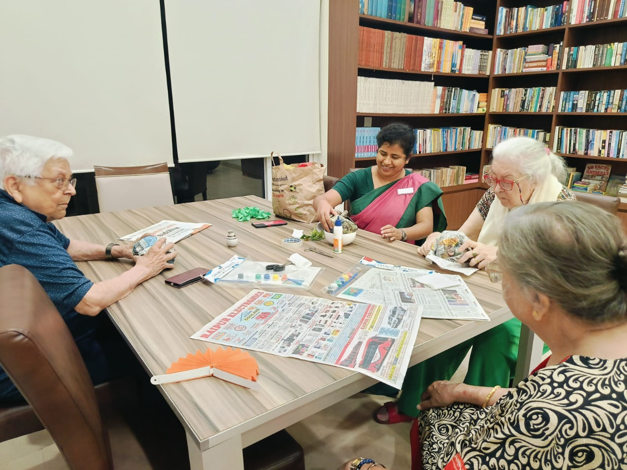 Senior citizens participating in an eco-friendly craft session at Jagriti dham - a luxurious old age home in Kolkata with a library backdrop.