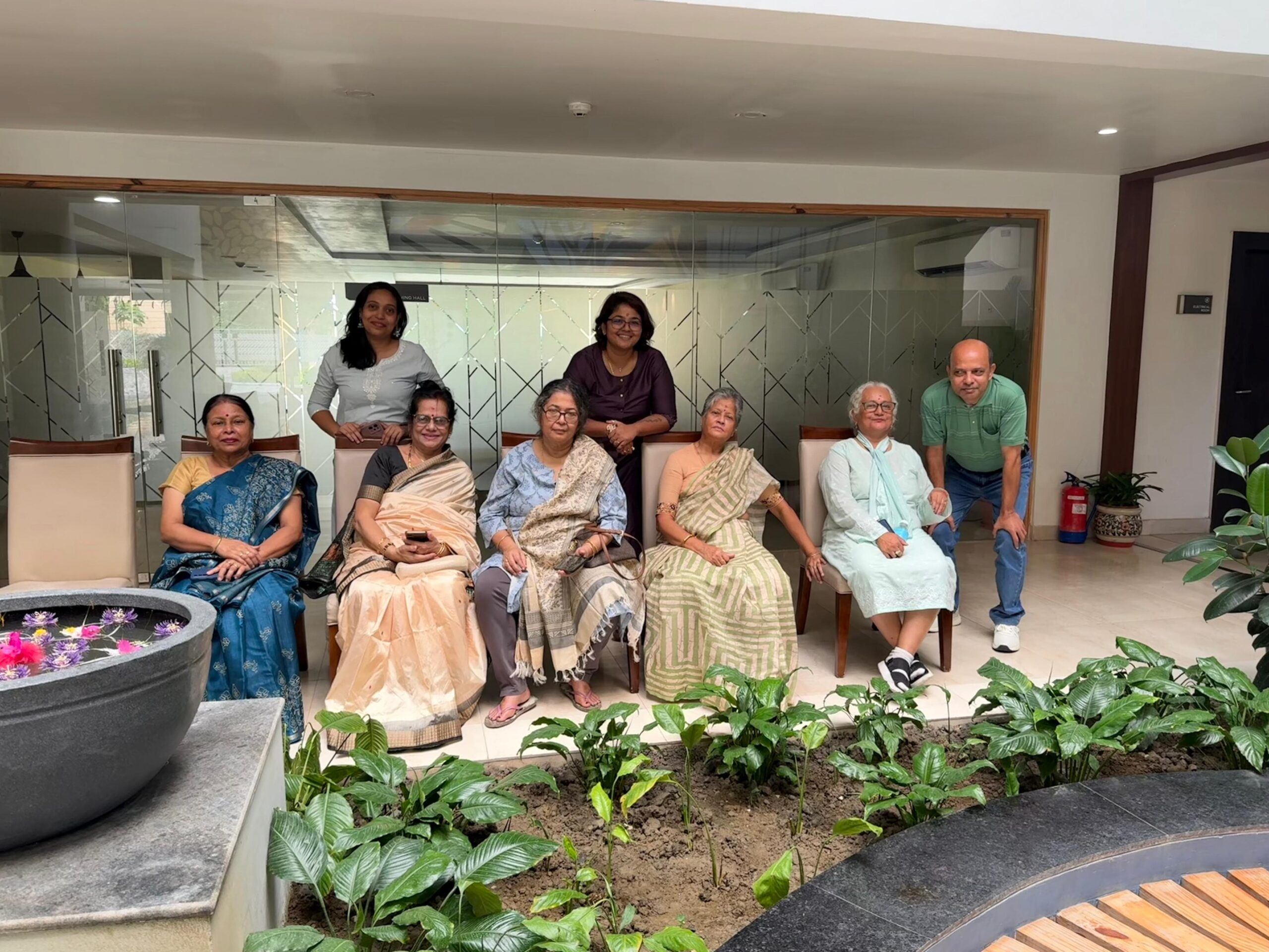 A group of smiling residents and guests posing for a photo in the pleasant, plant-filled lobby of Jagriti Dham during the Durga Puja festivities.