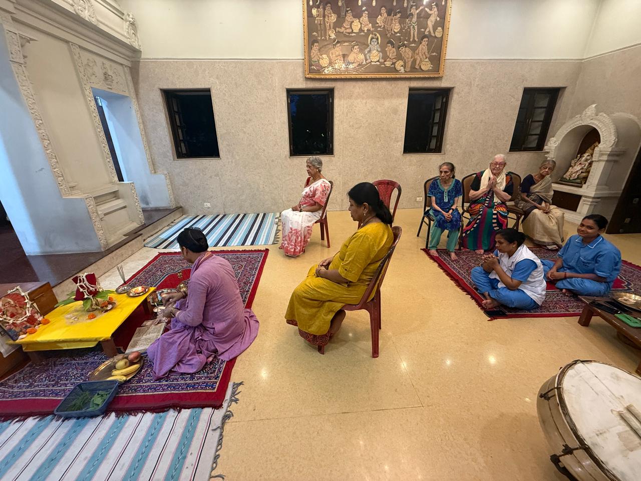 Senior residents and caregivers of Jagriti Dham gathered in the community hall, peacefully observing the Kojagari Laxmi Puja ceremony as it is performed, fostering a sense of shared devotion and community.