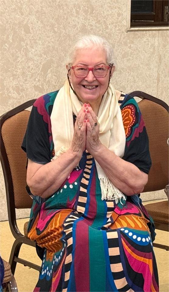 A joyful senior resident of Jagriti Dham, dressed in vibrant festive attire, smiles warmly at the camera with her hands joined in a prayerful gesture during the Laxmi Puja celebration.