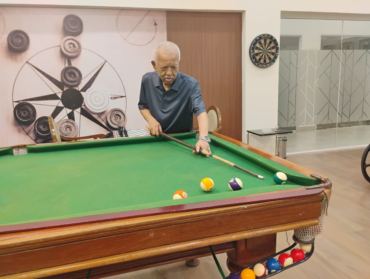 A senior resident enjoys a game of pool in the dedicated indoor games room at Jagriti Dham, showcasing the active lifestyle amenities at these luxury retirement homes in Kolkata.