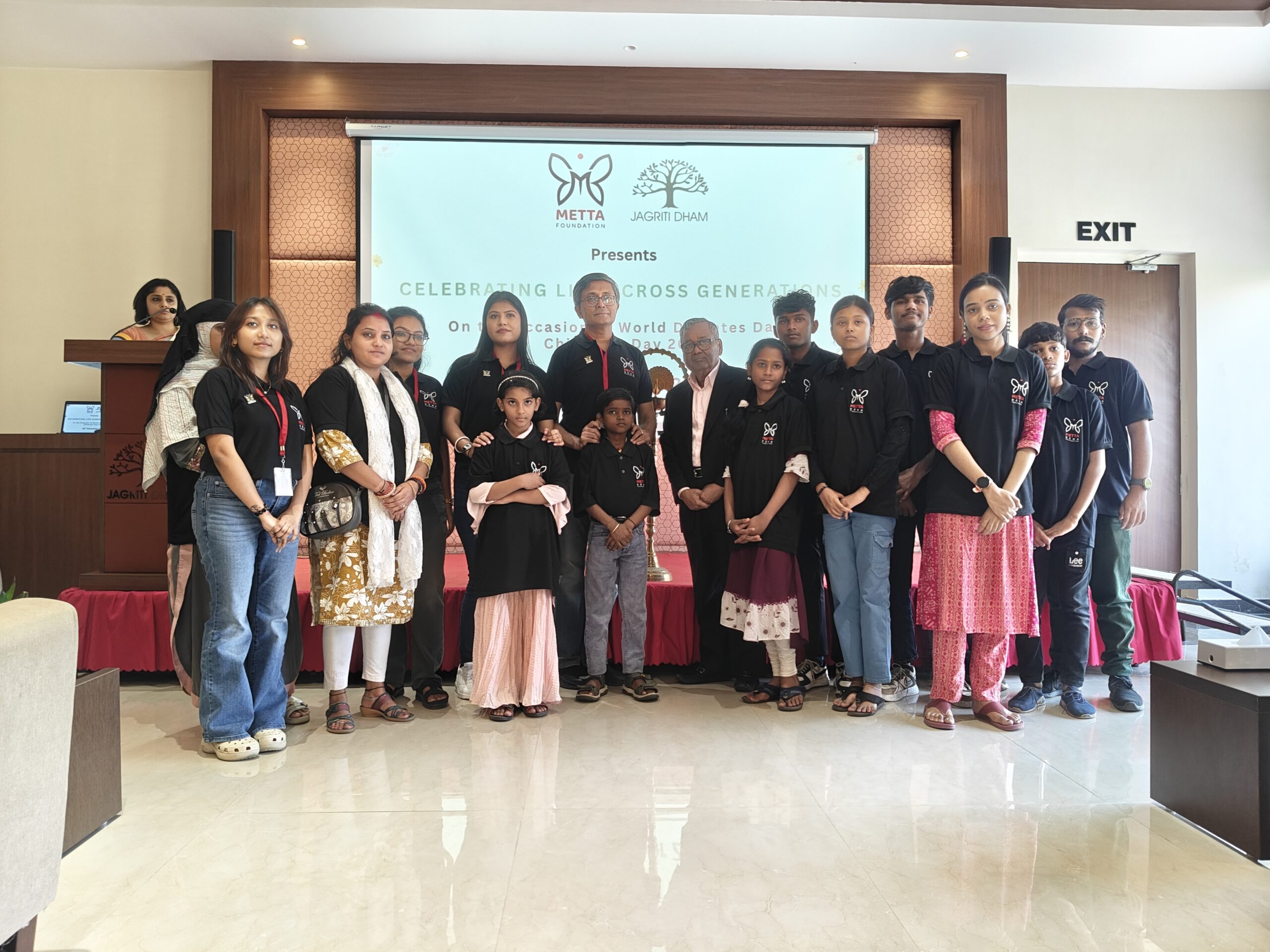 A group of adults and children posing for a photo on stage during the "Celebrating Life Across Generations" event hosted by Metta Foundation and Jagriti Dham.