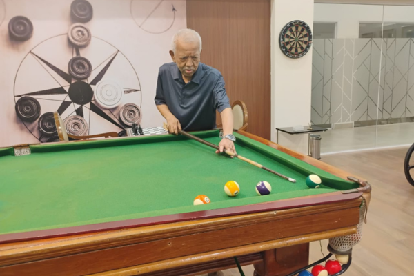 A senior resident enjoys a game of pool in the dedicated indoor games room at Jagriti Dham, showcasing the active lifestyle amenities at these luxury retirement homes in Kolkata.