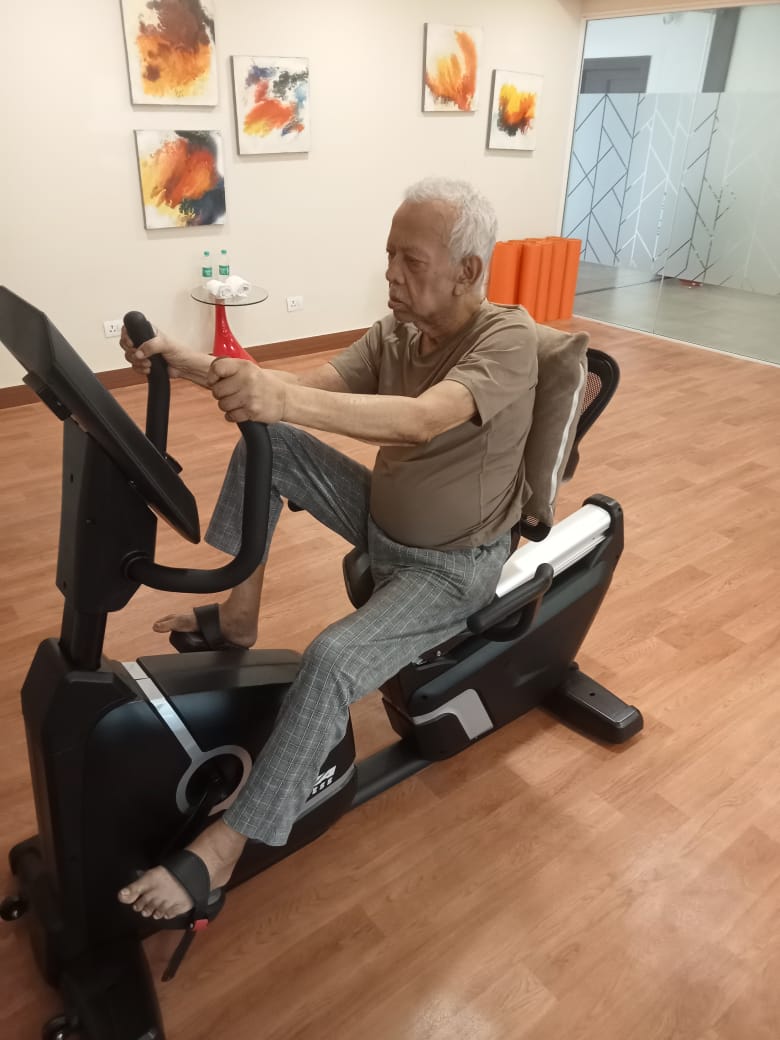 An elderly resident staying active by using a stationary recumbent bike in the fitness center at Jagriti Dham, a luxury old age home in Kolkata.