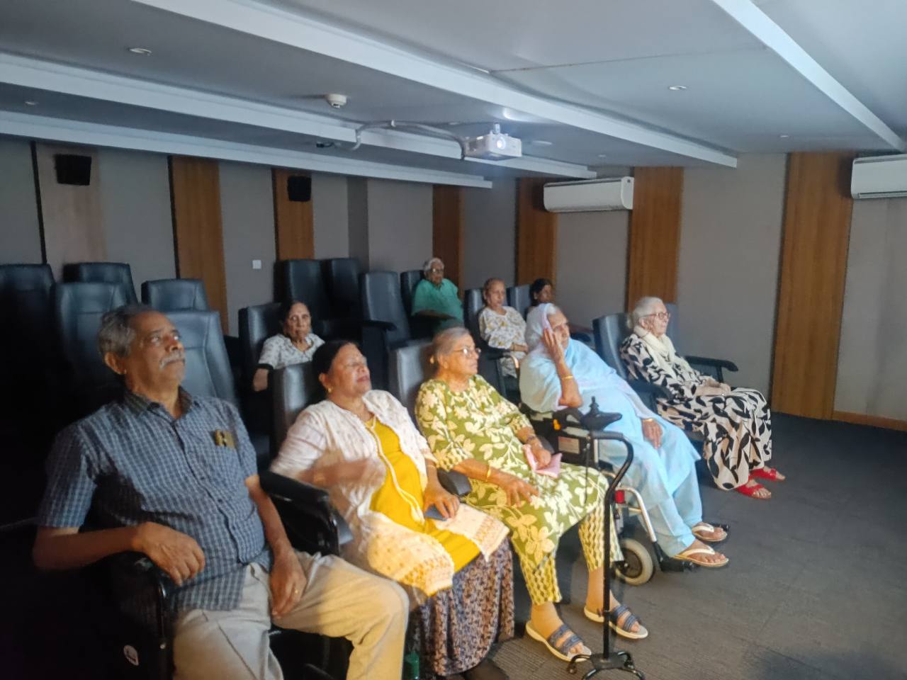 Seniors relaxing in recliners and watching a screening of classic Bengali movioe in the well-appointed theater room of Jagriti Dham, a luxurious old age home in Kolkata.