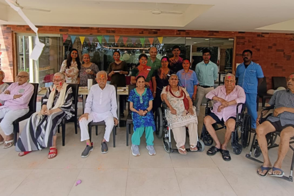 A joyful group portrait of residents and caregiving staff at Jagriti Dham gathered together like a family for Holi 2026.