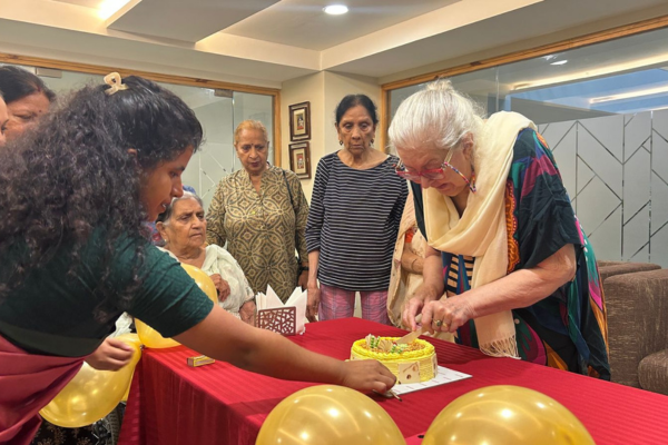 An elderly resident cuts a birthday cake surrounded by peers and staff at Jagriti Dham, highlighting the resident-centric events hosted in premium senior living communities.