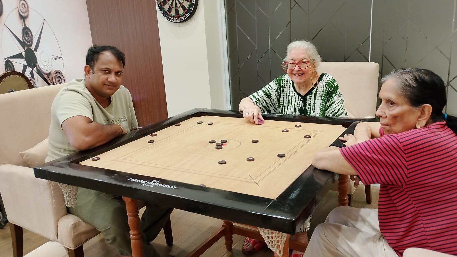 Happy residents of Jagriti Dham senior living community enjoying an active indoor game of carrom in the luxury recreational games room.