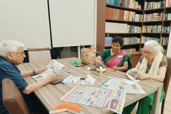 Senior residents engaging in an arts and crafts activity with a supportive staff member inside a well-stocked library room at a premium retirement home offering senior citizen care services.
