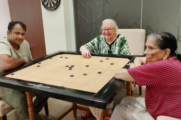 Happy residents of Jagriti Dham senior living community enjoying an active indoor game of carrom in the luxury recreational games room.