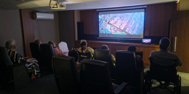 People seated in a small theater room watching a movie projected on a large screen.