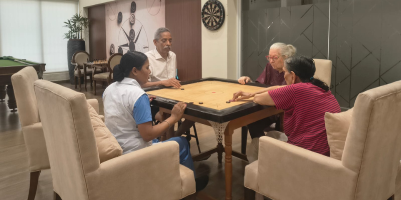 Residents and a caregiver enjoy a game of carrom in a recreation room at one of the best old age homes in Kolkata, promoting social engagement and active ageing.