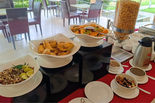 A nutritious buffet spread showcasing healthy food for the elderly, including fresh bananas, cut papaya, sprouts, nuts, and cereal inside a senior living dining hall.