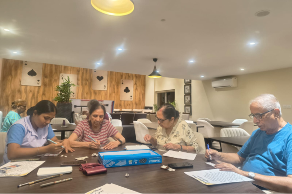 Senior residents playing Tambola board games with caregiver assistance at an assisted living facility in Kolkata.