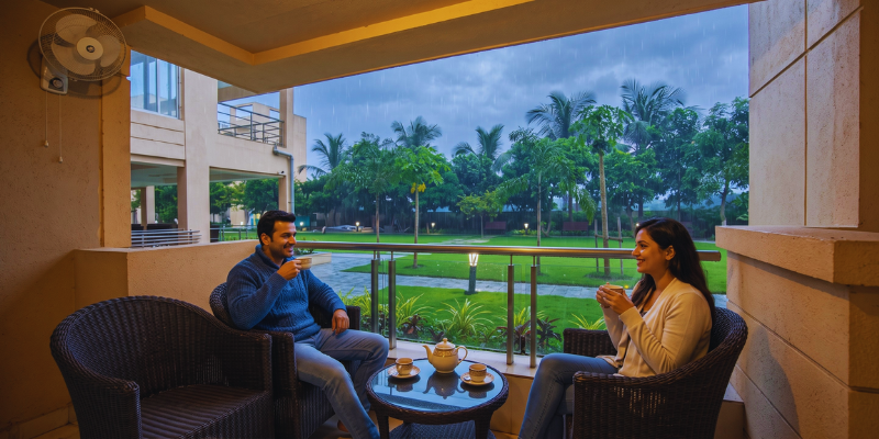 A young couple sitting in wicker armchairs drinking tea on a private balcony overlooking lush green gardens at a luxury bed and breakfast.