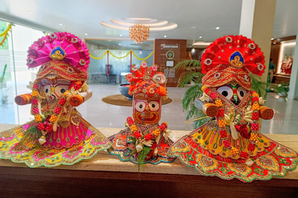 Three beautifully adorned wooden idols of Lord Jagannath, Goddess Subhadra, and Lord Balabhadra wearing vibrant, ornate traditional attire on display.