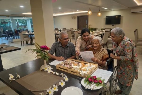 A group of seniors and a young woman review documents around a table in a bright dining room.