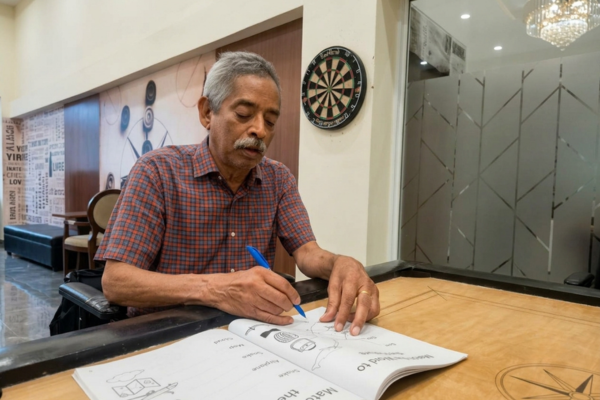 An elderly man engaged in cognitive activity worksheets inside an indoor recreation room at Jagriti Dham.