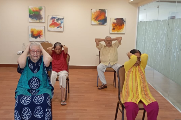Elderly individuals doing seated head and neck stretches in a senior living with a medical care facility.