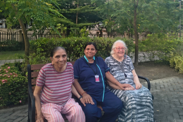 Two senior women seated with a caregiver on a garden bench, showcasing the community spirit in independent and assisted living.