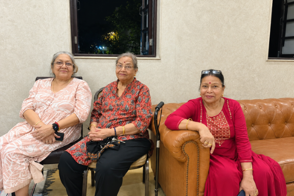 Three elderly women sitting together on a sofa and chairs in a comfortable indoor setting at Jagriti Dham.