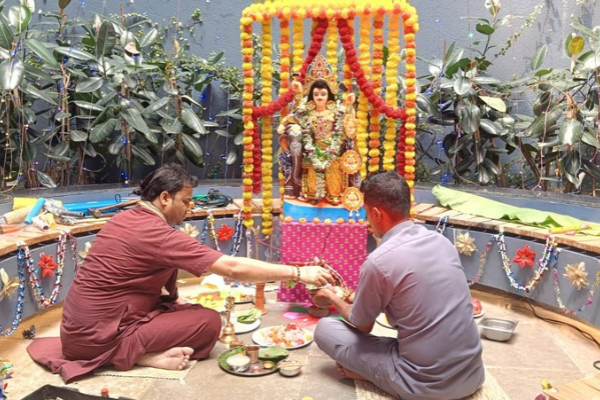 Two men performing a traditional Hindu puja and ritual in front of a decorated idol surrounded by marigold garlands at an old age home.