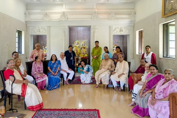 A group of elderly residents, family members, and caregivers gathered together inside a spacious living room at an old age home.